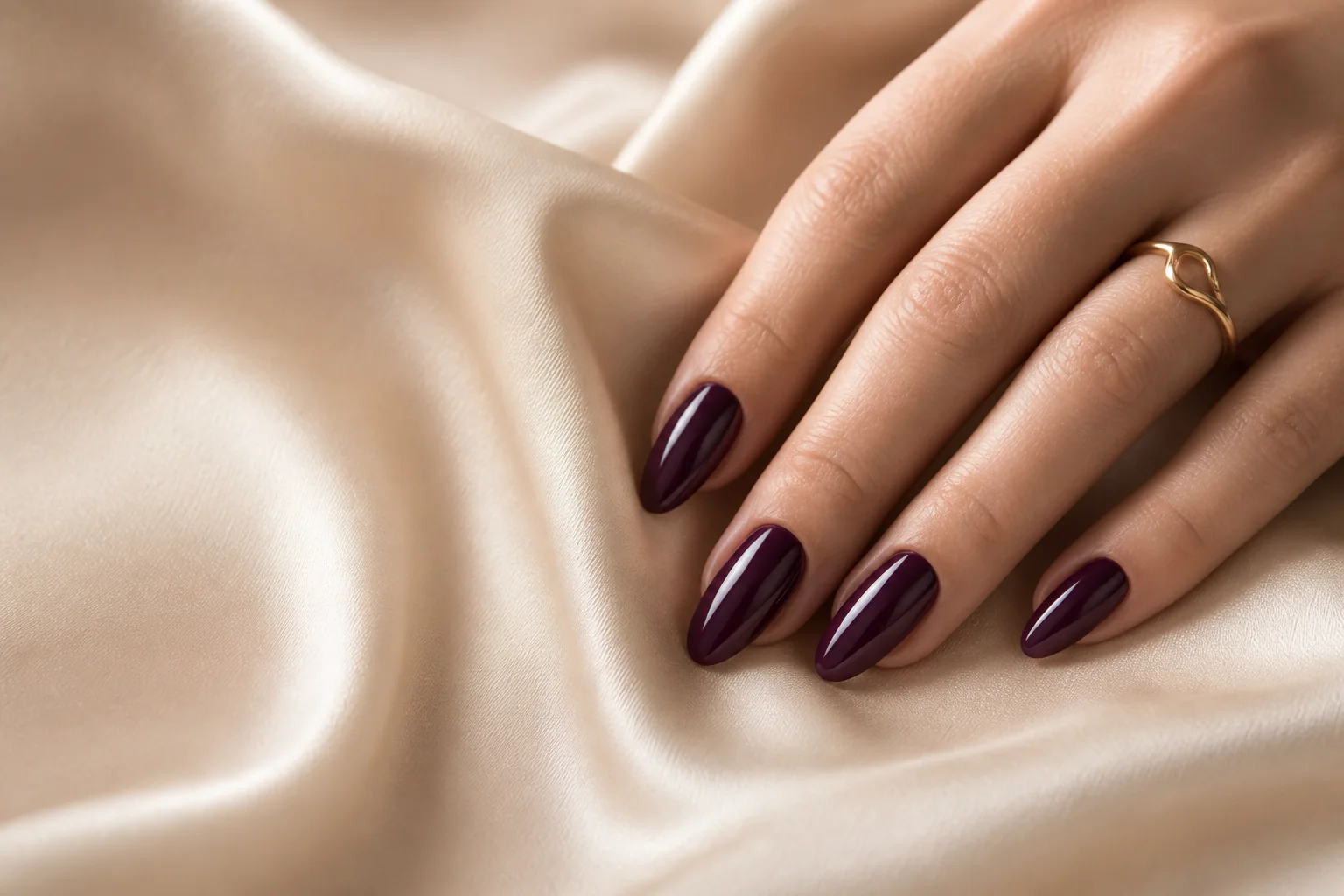 Deep aubergine almond-shaped nails resting on softly folded champagne silk in the VELOURA showcase.